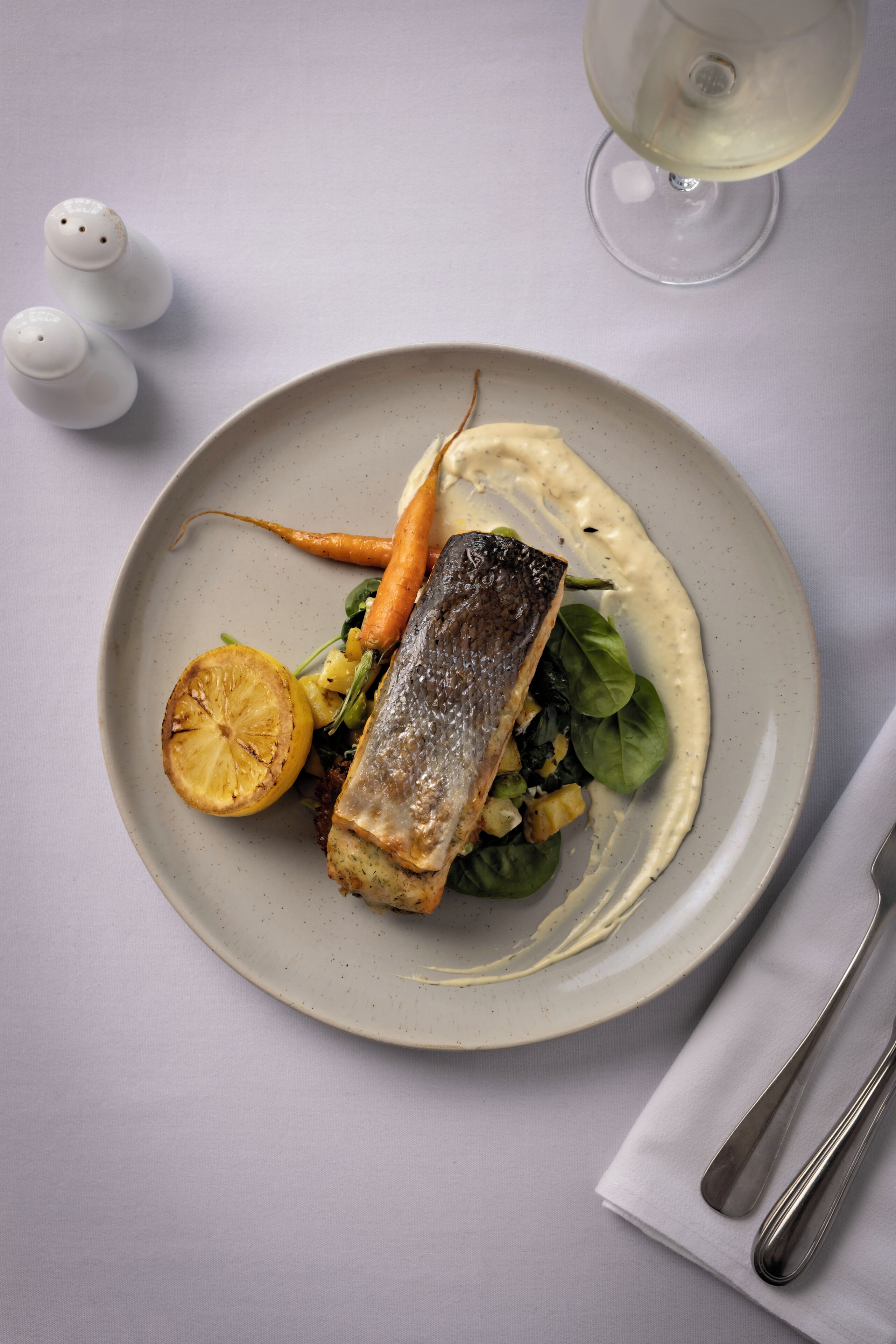A plate of food with a fish, vegetables, and a lemon slice.