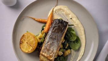 A plate of food with a fish, vegetables, and a lemon slice.