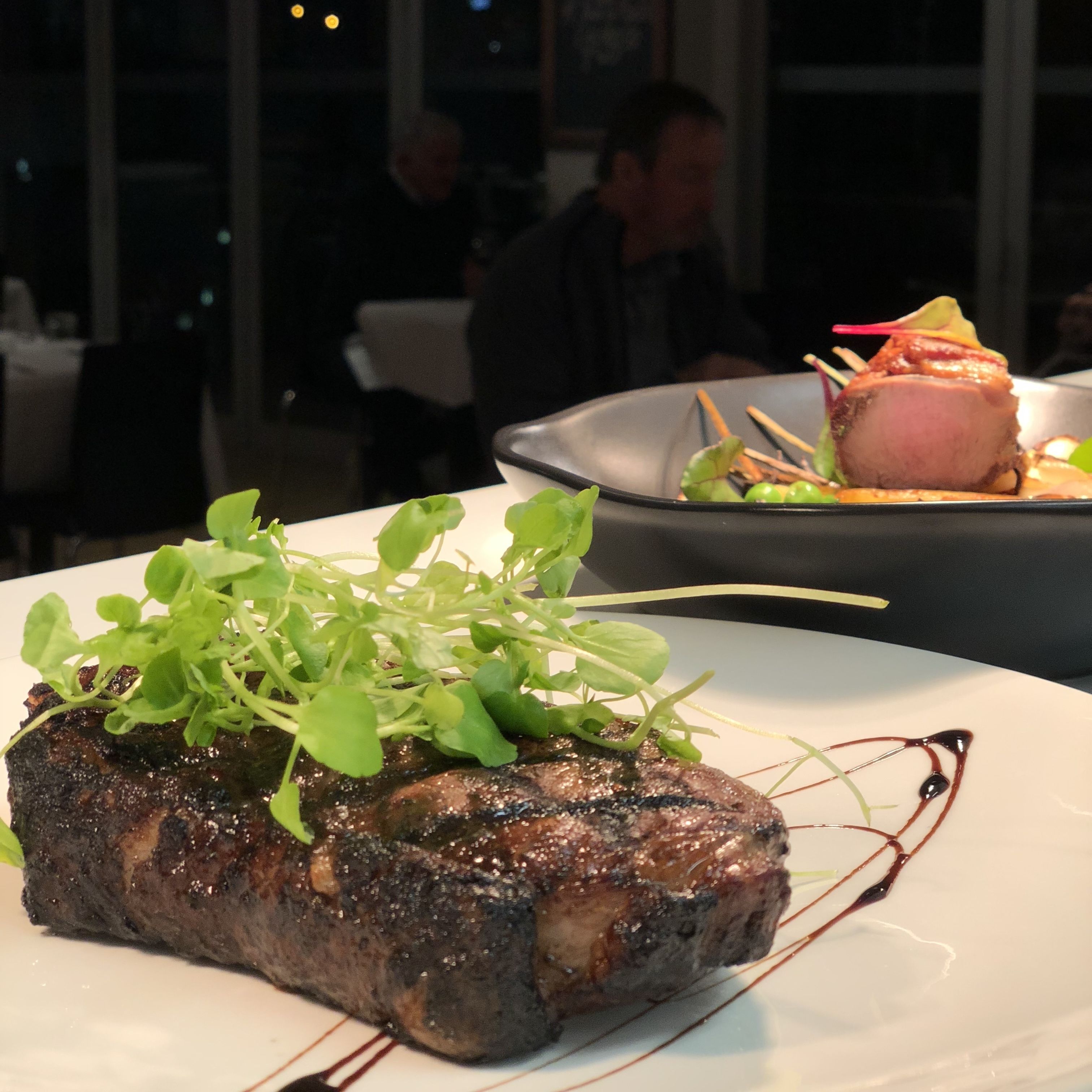 A steak with greens on a plate, in a restaurant setting.