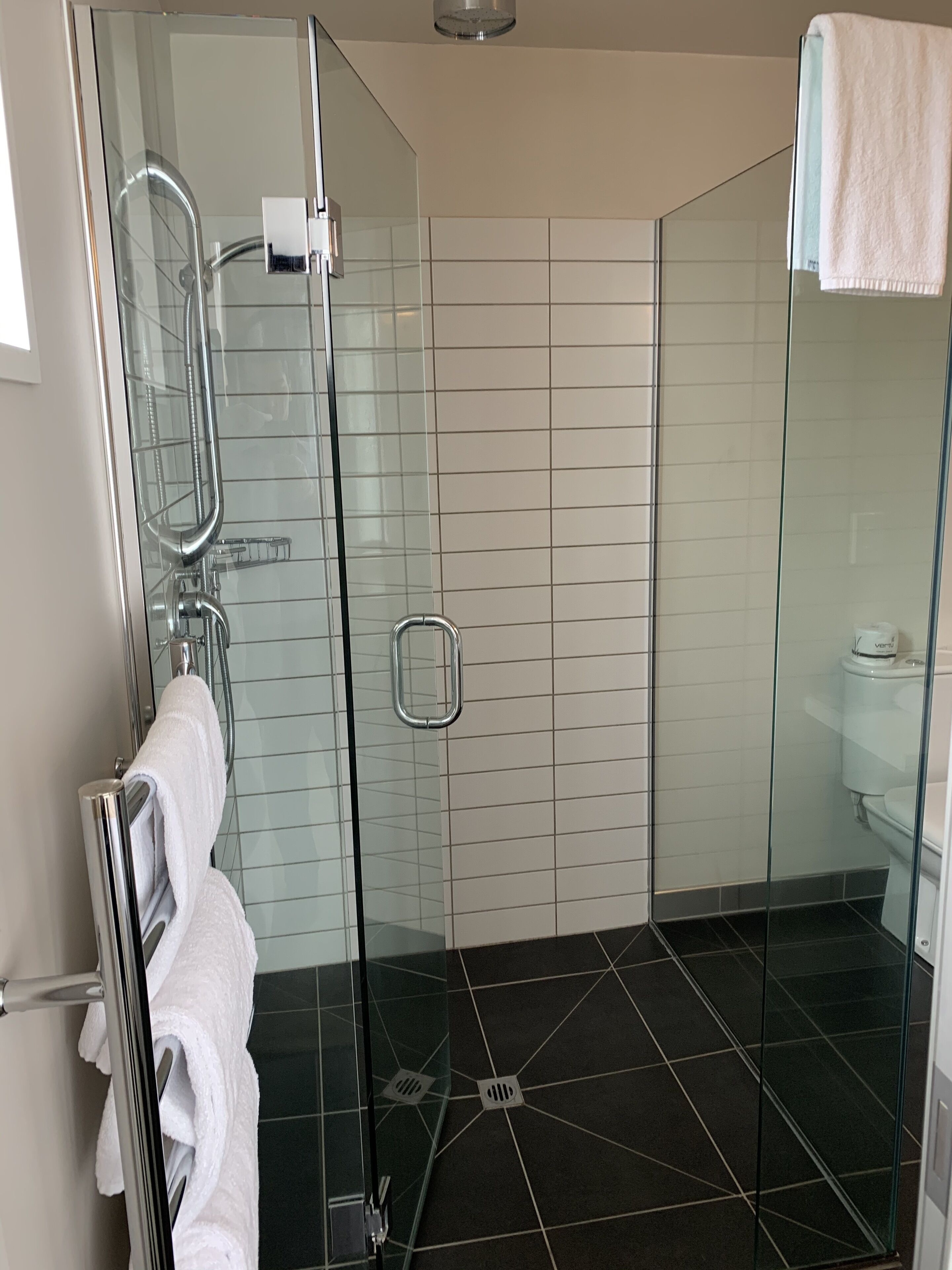 Un baño moderno con cabina de ducha de vidrio, un perchero blanco y un inodoro.