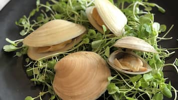 A black plate with clams and green microgreens.