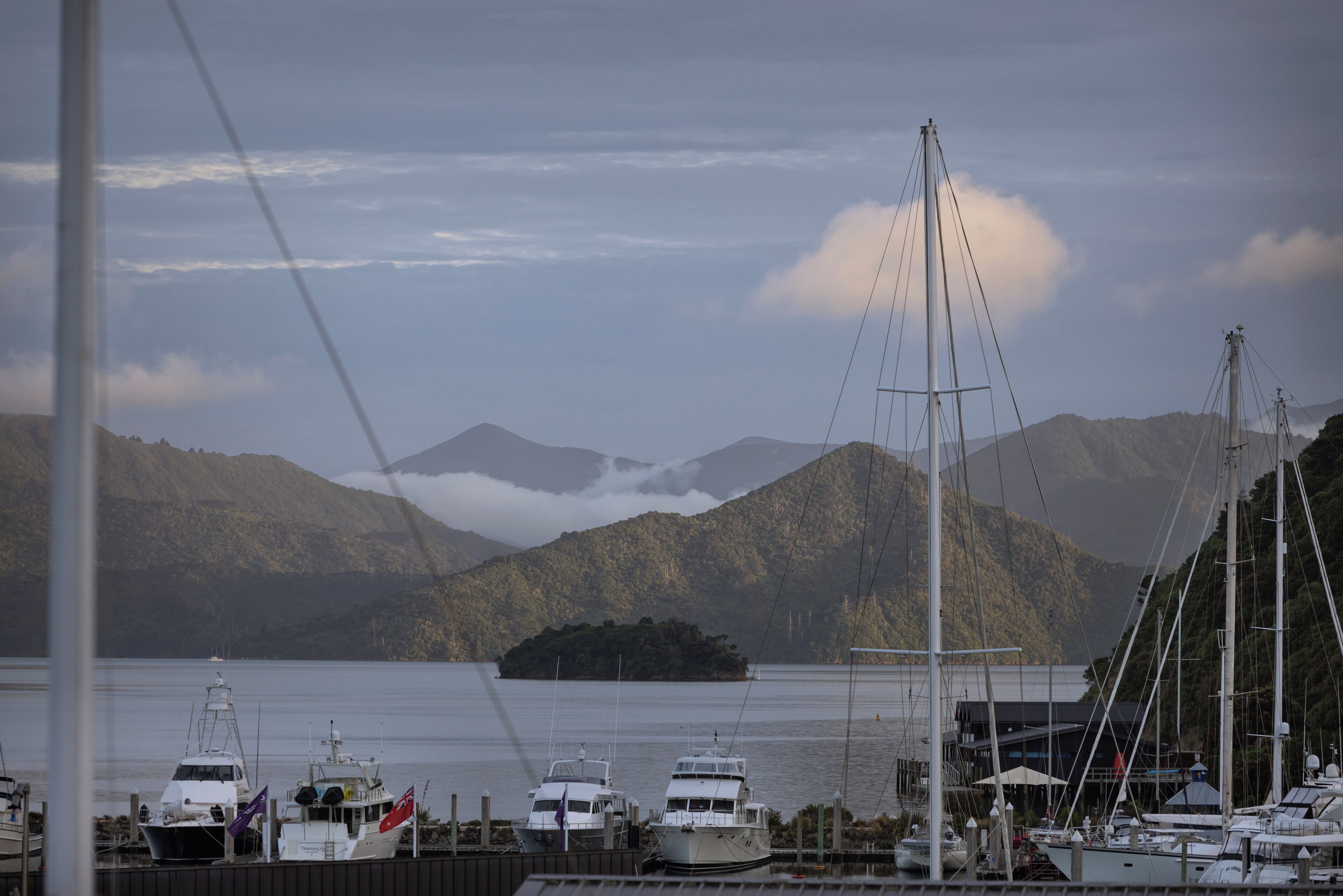 A marina with boats docked, a mountainous backdrop, and a small island in the distance.