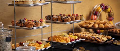 Un bufé con múltiples bandejas de pasteles, muffins y fruta.