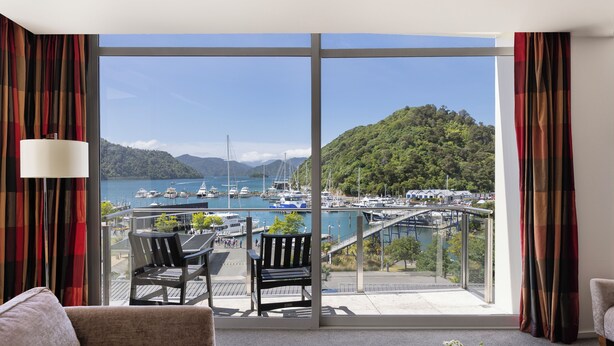 Un balcone con vista su un porto turistico, un tavolo di legno, due sedie e un divano.