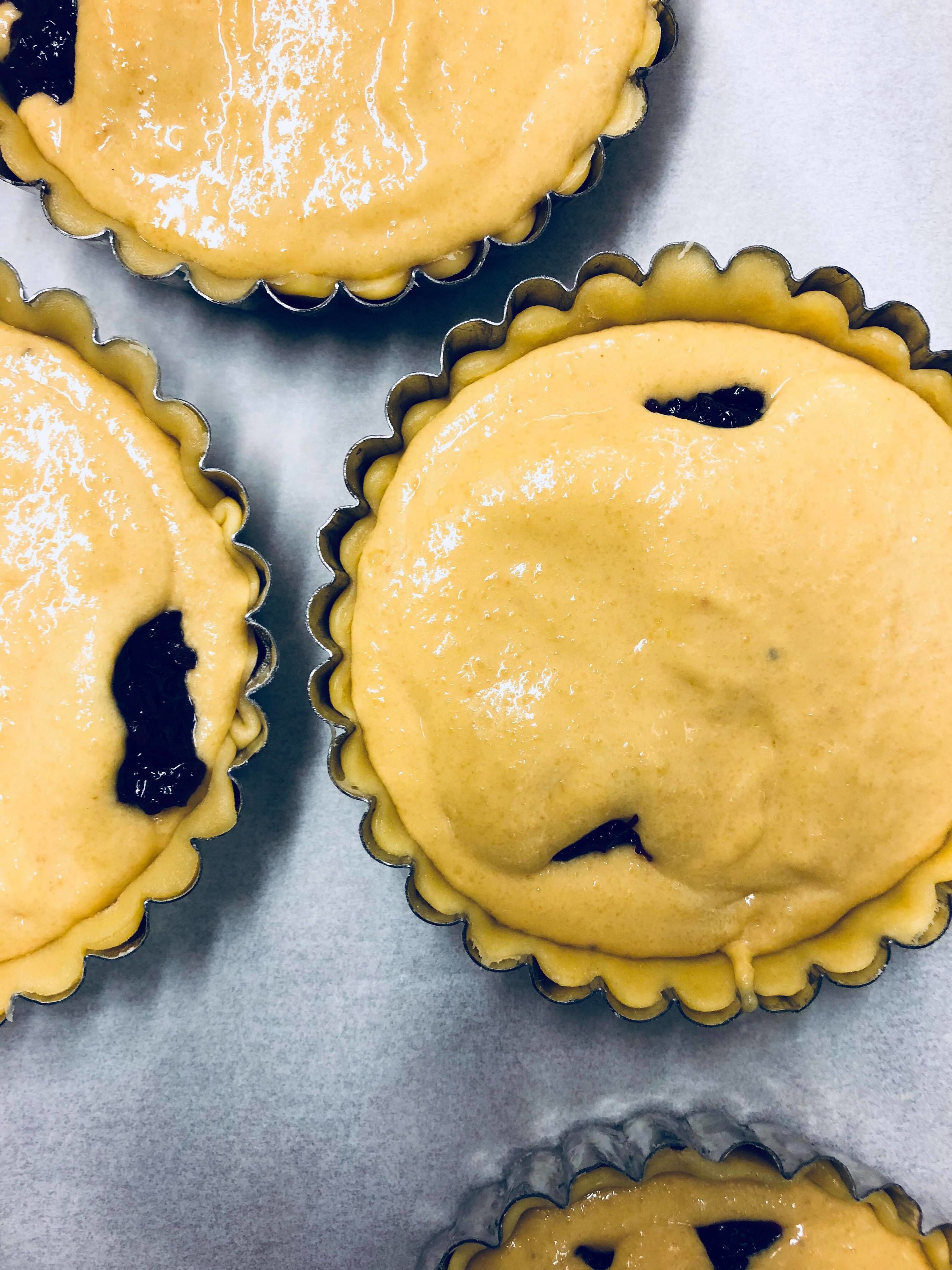 Cuatro masas para tarta con una corteza dorado-café y un relleno oscuro, presumiblemente de arándanos, sobre una bandeja para hornear.