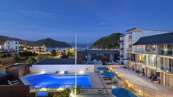 Relax by the rooftop pool surrounded by lounge chairs and umbrellas, with scenic views of the surrounding landscape and water.