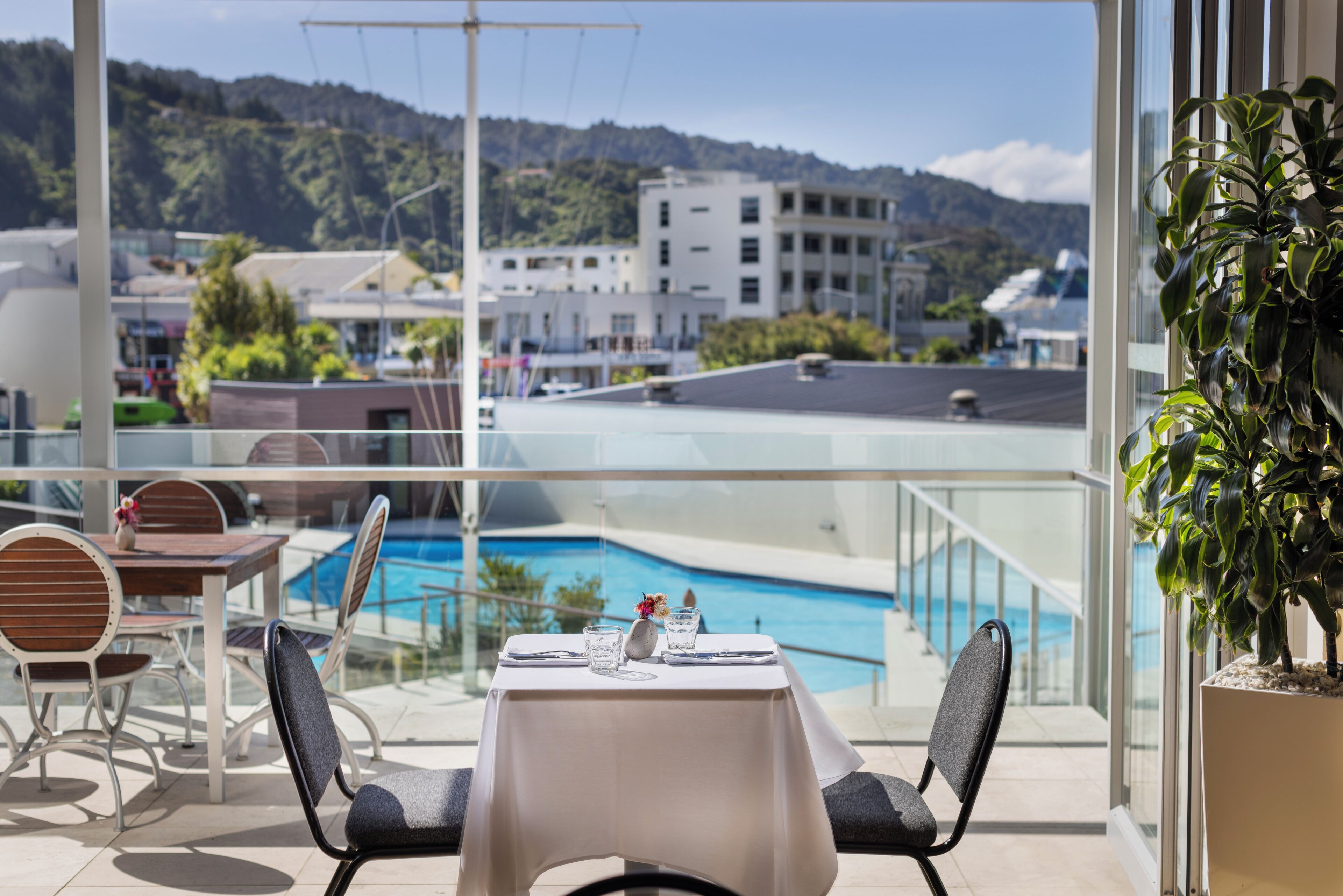 Un balcon avec une table et des chaises, donnant sur une piscine et un immeuble d’où l’on peut admirer les collines.