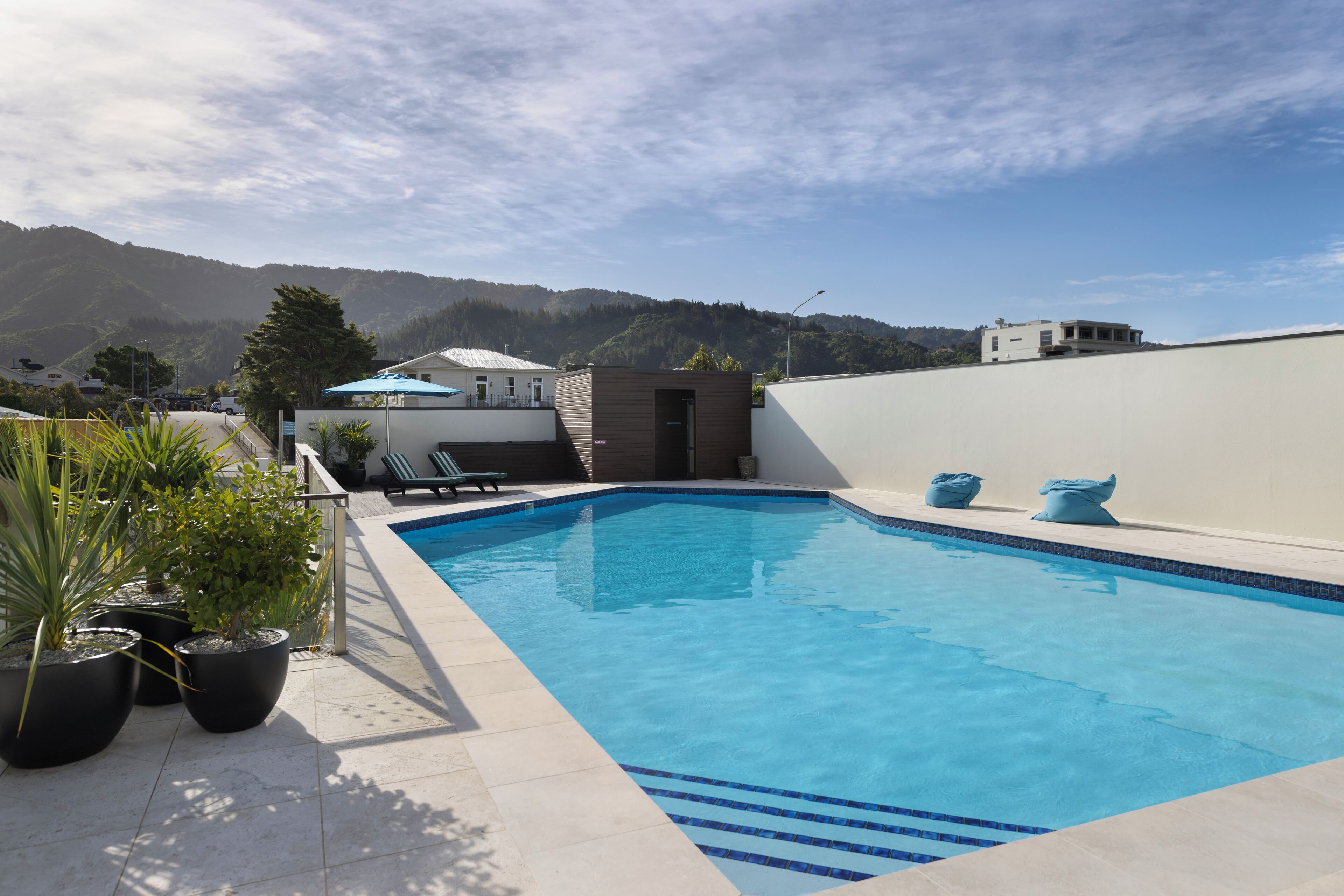 A swimming pool with a view of mountains, potted plants, and a small building with a door.