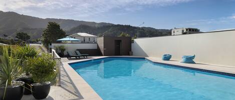 A swimming pool with a view of mountains, potted plants, and a small building with a door.