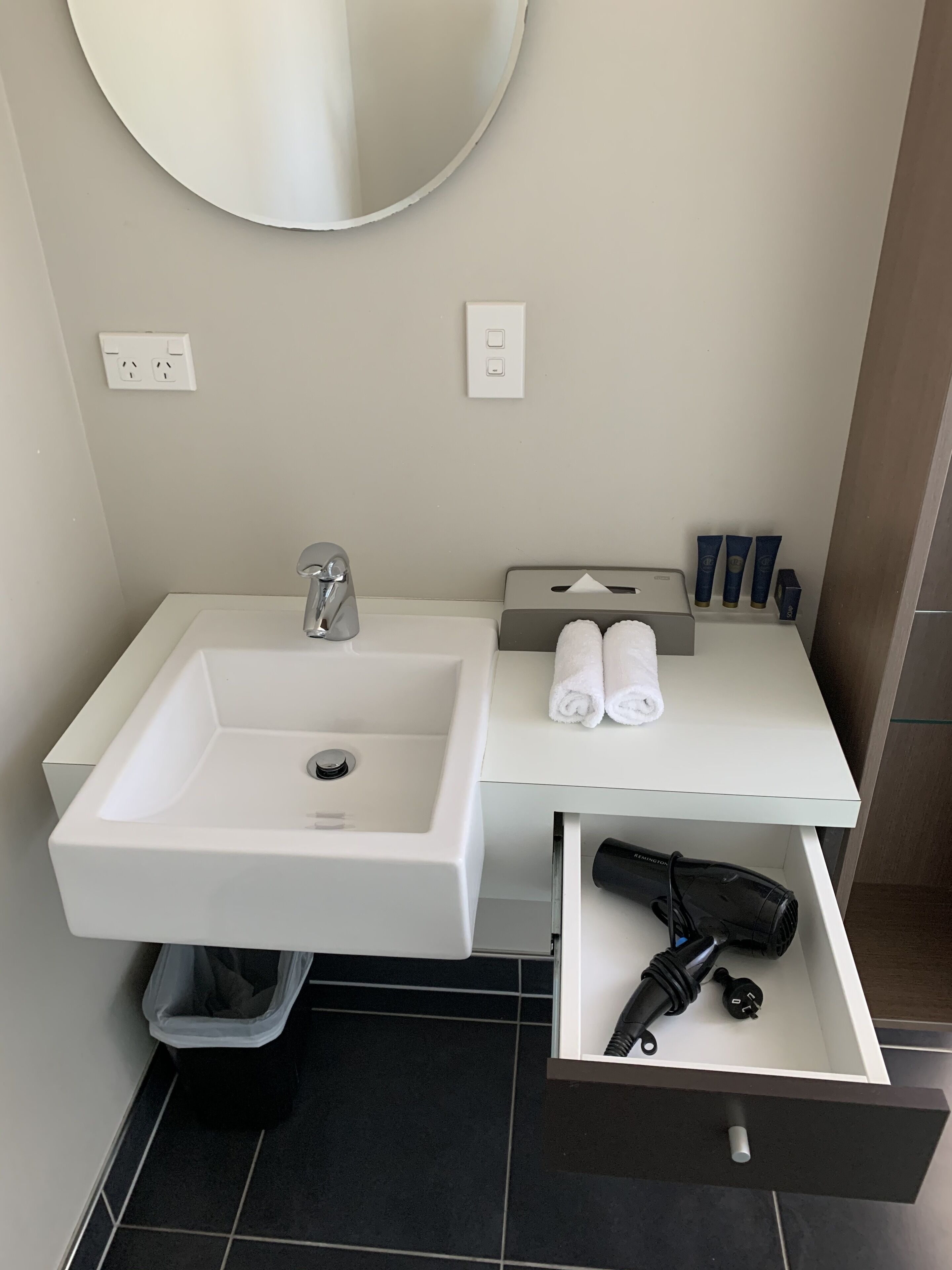 Ein modernes Badezimmer mit Waschbecken, Spiegel, Handtuchhalter und Fön in einer Schublade.