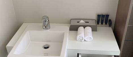Ein modernes Badezimmer mit Waschbecken, Spiegel, Handtuchhalter und Fön in einer Schublade.