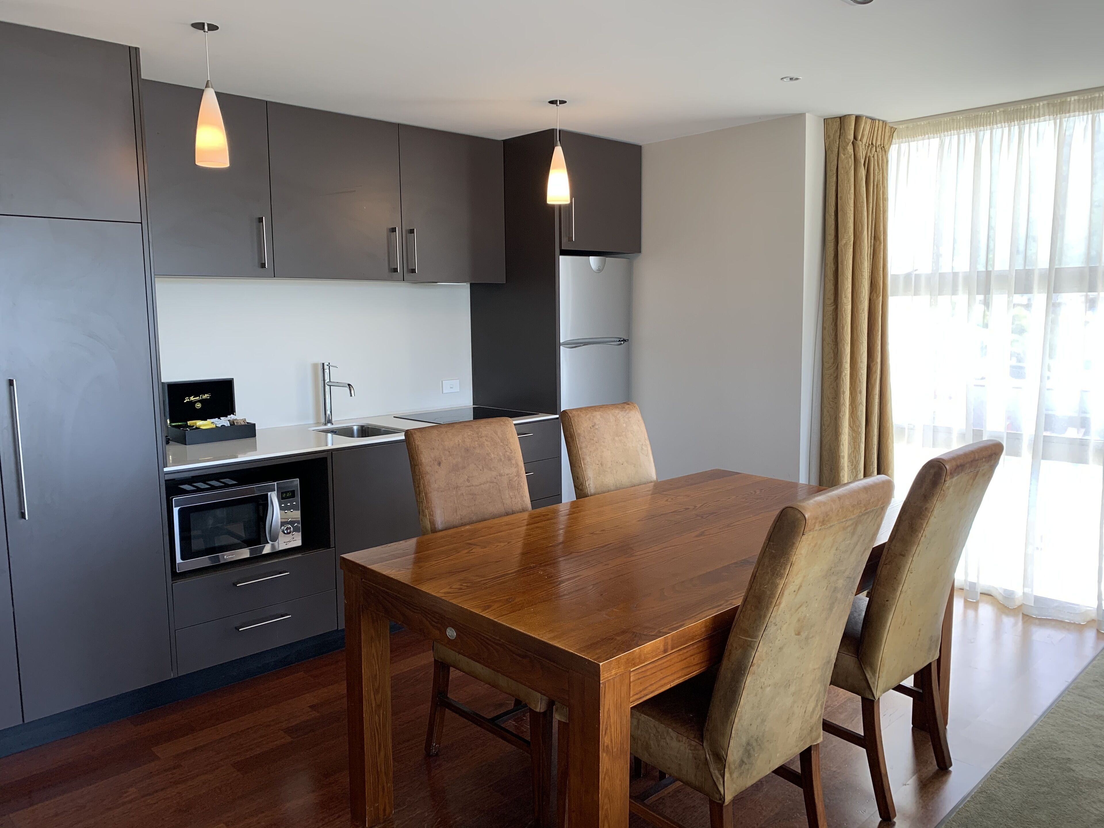 Una cocina moderna con armarios oscuros, una mesa de comedor de madera y un horno empotrado.