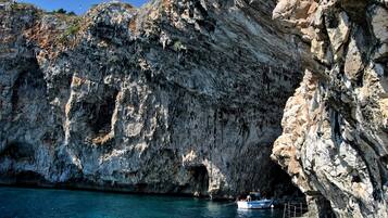 Zona costera rocosa con un barco anclado cerca de la entrada de una cueva.