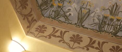 A corner of a room with a decorative floral pattern on the wall and a light fixture.