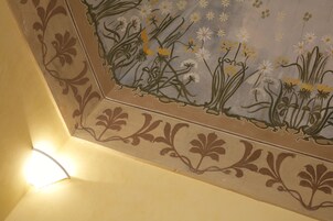 A corner of a room with a decorative floral pattern on the wall and a light fixture.
