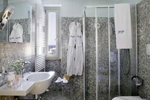 Un baño con un lavamanos grande, una cabina de ducha de vidrio y dos albornoces blancos con el bordado 'PGP'.