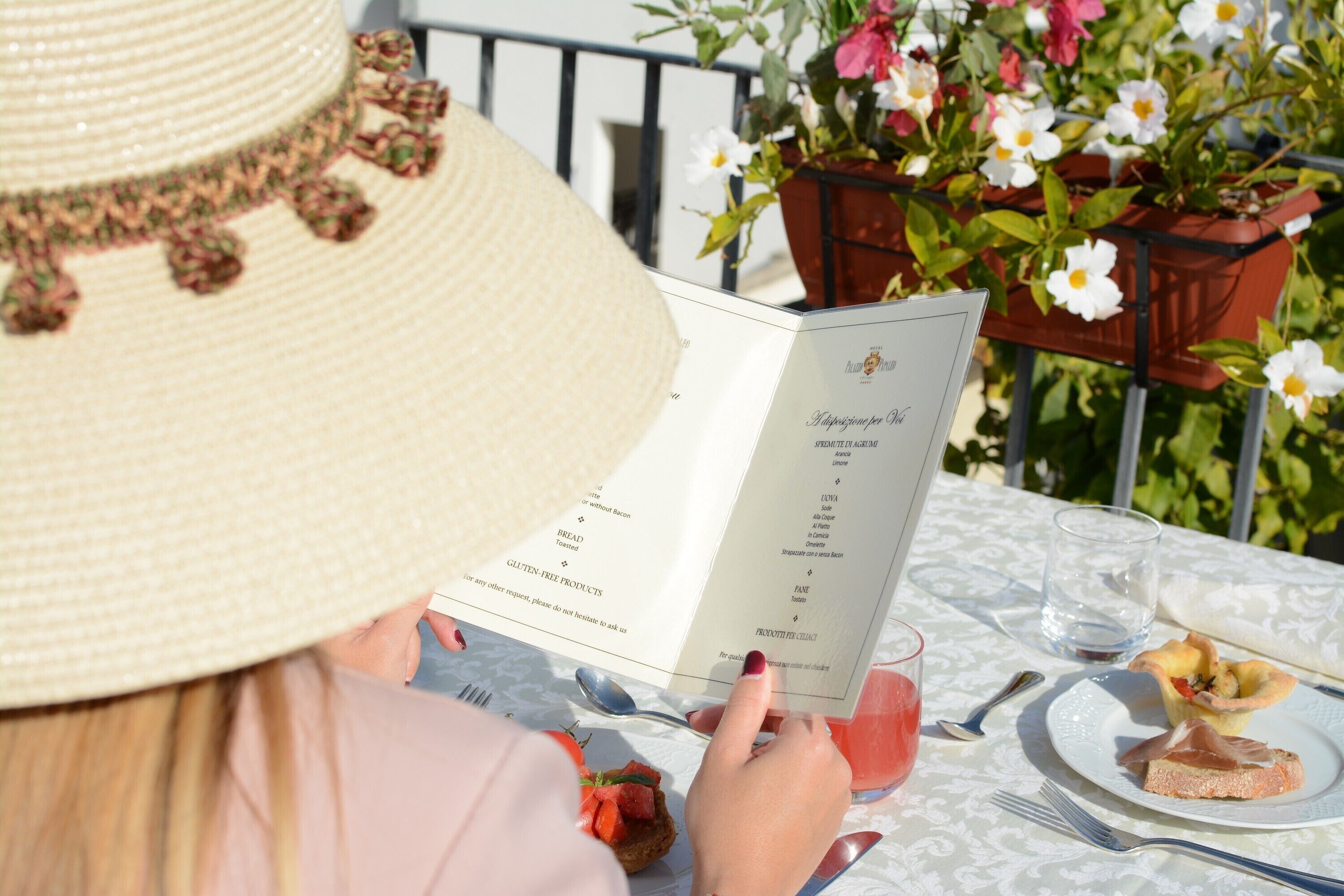 Una persona leyendo un menú en una mesa al aire libre, con una planta en maceta y flores al fondo.