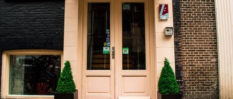 L’entrée d’un hôtel, avec une porte à deux battants, portant le numéro 25, et un tapis rouge qui mène à l’intérieur.
