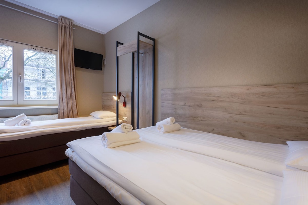 A hotel room with two beds, a TV mounted on the wall, and a window with curtains.