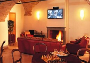 Un salón acogedor con chimenea, un televisor montado en la pared y una zona de comedor con un tablero de ajedrez.