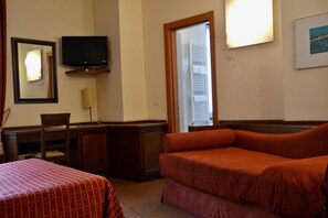 Habitación de hotel con dos camas, un escritorio, una silla, un televisor y una ventana con contraventanas.