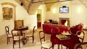 A cozy room with a high arched ceiling, a fireplace, a television, and a dining area with chairs and a table. - Hotel Italia (Foligno)