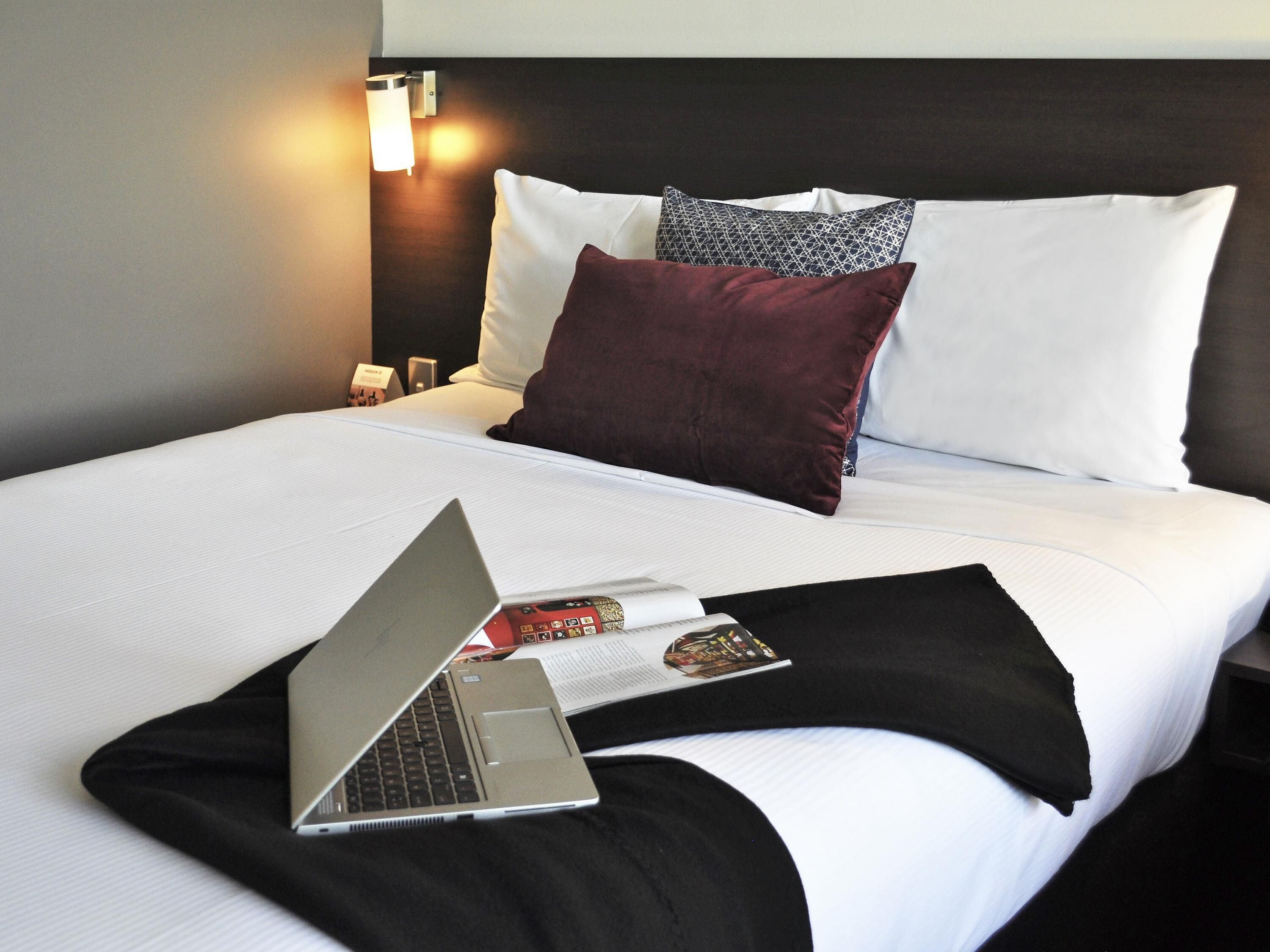 Un lit bien fait, avec un ordinateur portable, une télécommande et un magazine posés dessus.