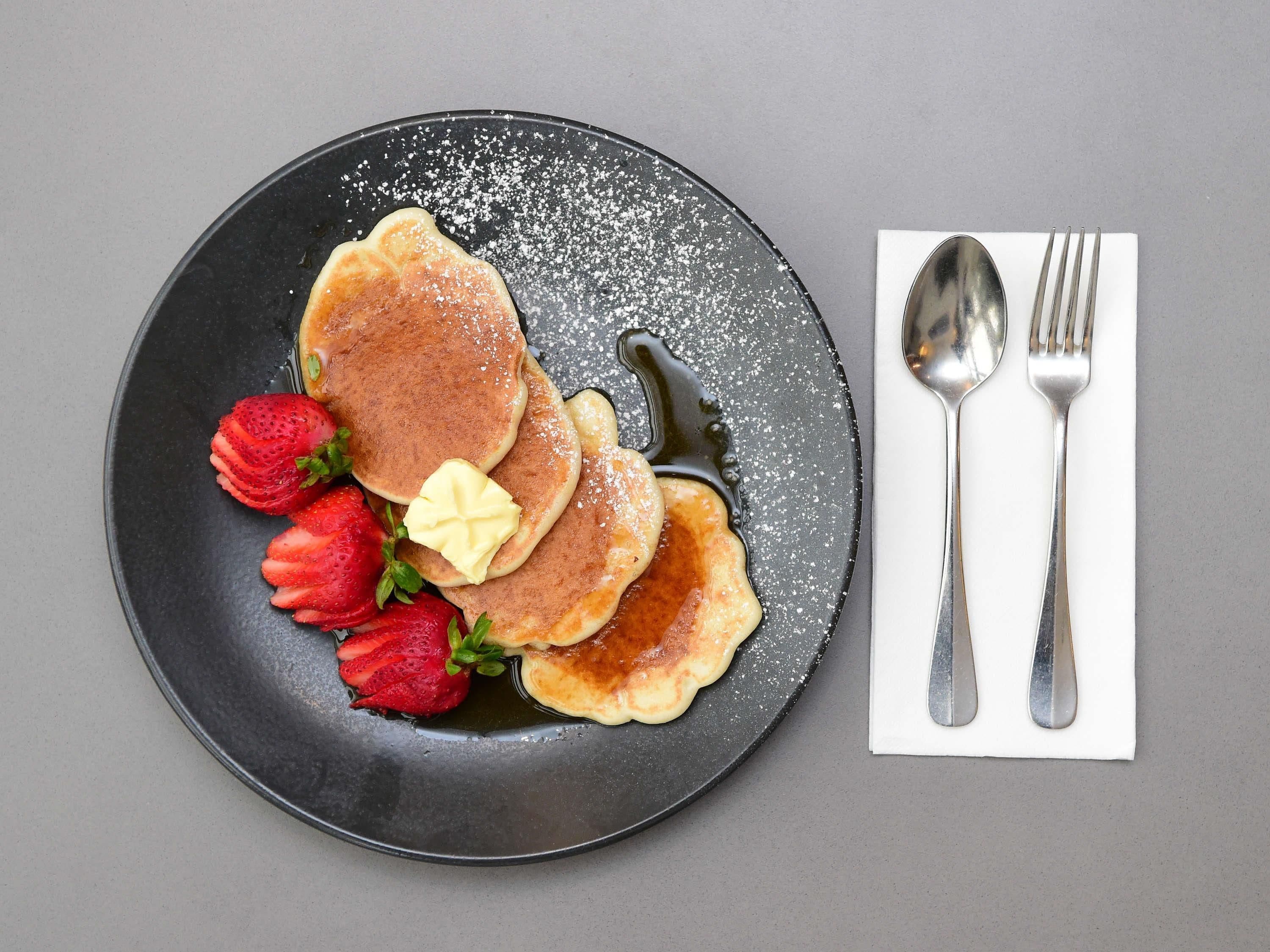 Une assiette avec des crêpes, des fraises et du beurre, le tout présenté sur une assiette foncée.