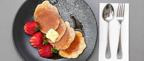 Une assiette avec des crêpes, des fraises et du beurre, le tout présenté sur une assiette foncée.