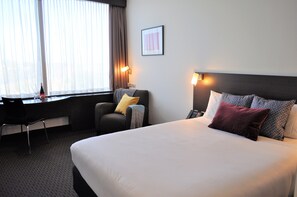 Une chambre d’hôtel avec un lit, un bureau, une chaise et une fenêtre avec des rideaux.