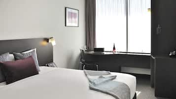 Una habitación de hotel con una cama grande, un escritorio con una computadora portátil, una silla y un refrigerador.