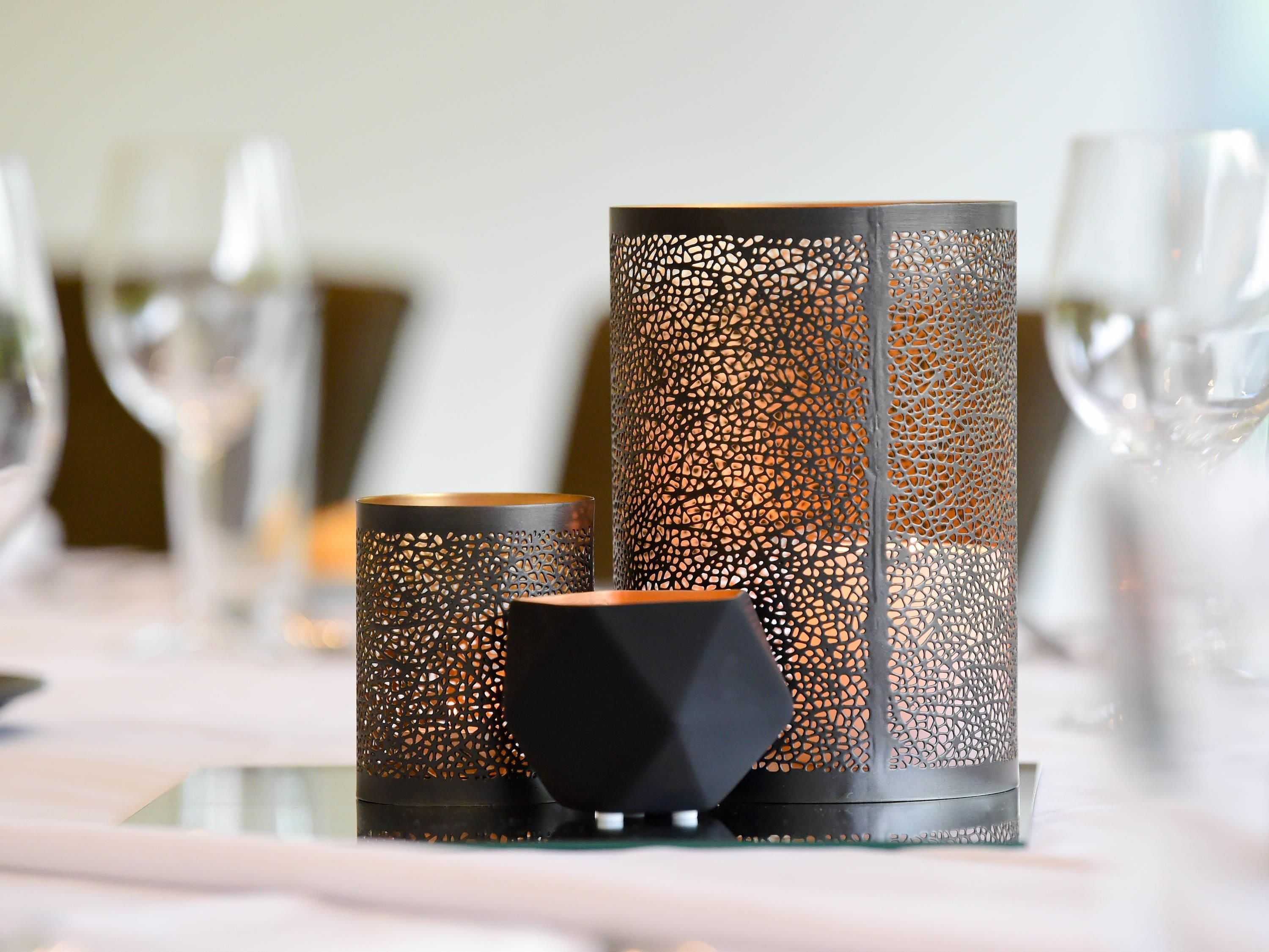 Three candle holders with intricate cut-out patterns on a table.