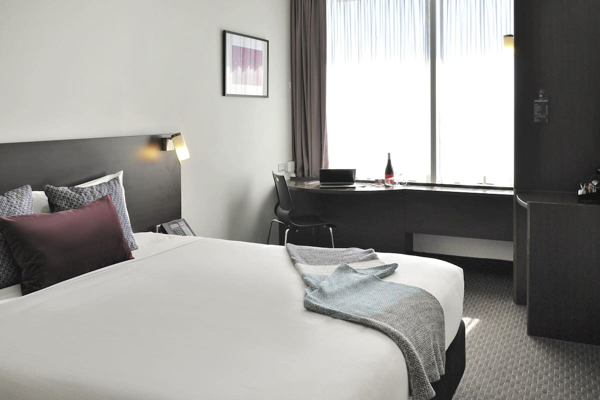 Ein Hotelzimmer mit einem großen Bett, einem Schreibtisch mit einem Laptop, einem Stuhl und einem Kühlschrank.