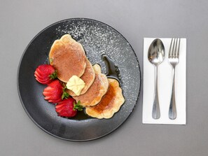 Une assiette avec des crêpes, des fraises et du beurre, le tout présenté sur une assiette foncée.