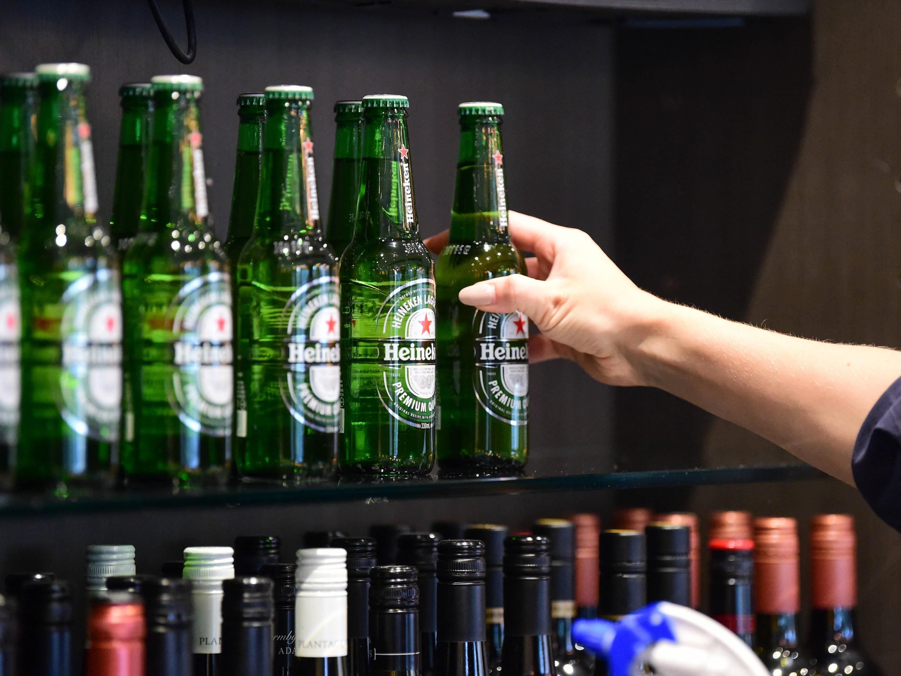 A hand holding a Heineken beer bottle with others on a shelf.