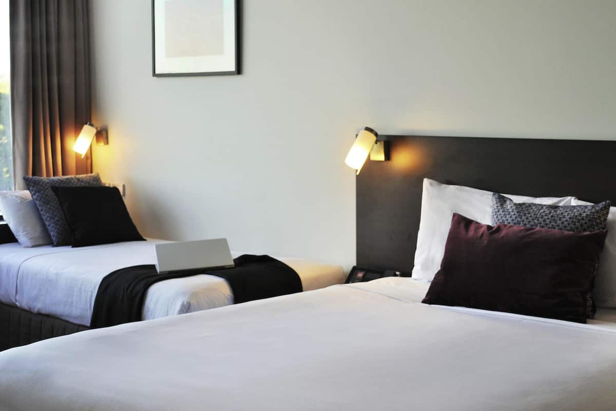 Ein Hotelzimmer mit zwei Betten, einem Laptop auf einem Bett und zwei Wandleuchten.