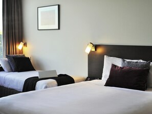 Une chambre d’hôtel avec deux lits, un ordinateur portable posé sur l’un des lits et deux lampes fixées au mur.