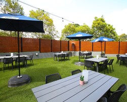 An outdoor patio area with multiple tables and chairs, blue umbrellas, and a wooden fence.