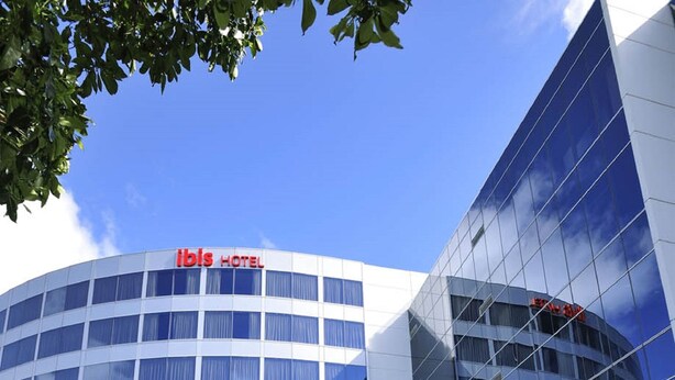 Ein modernes Hotelgebäude mit einem gut sichtbaren 'ibis HOTEL'-Schild vor der Fassade.