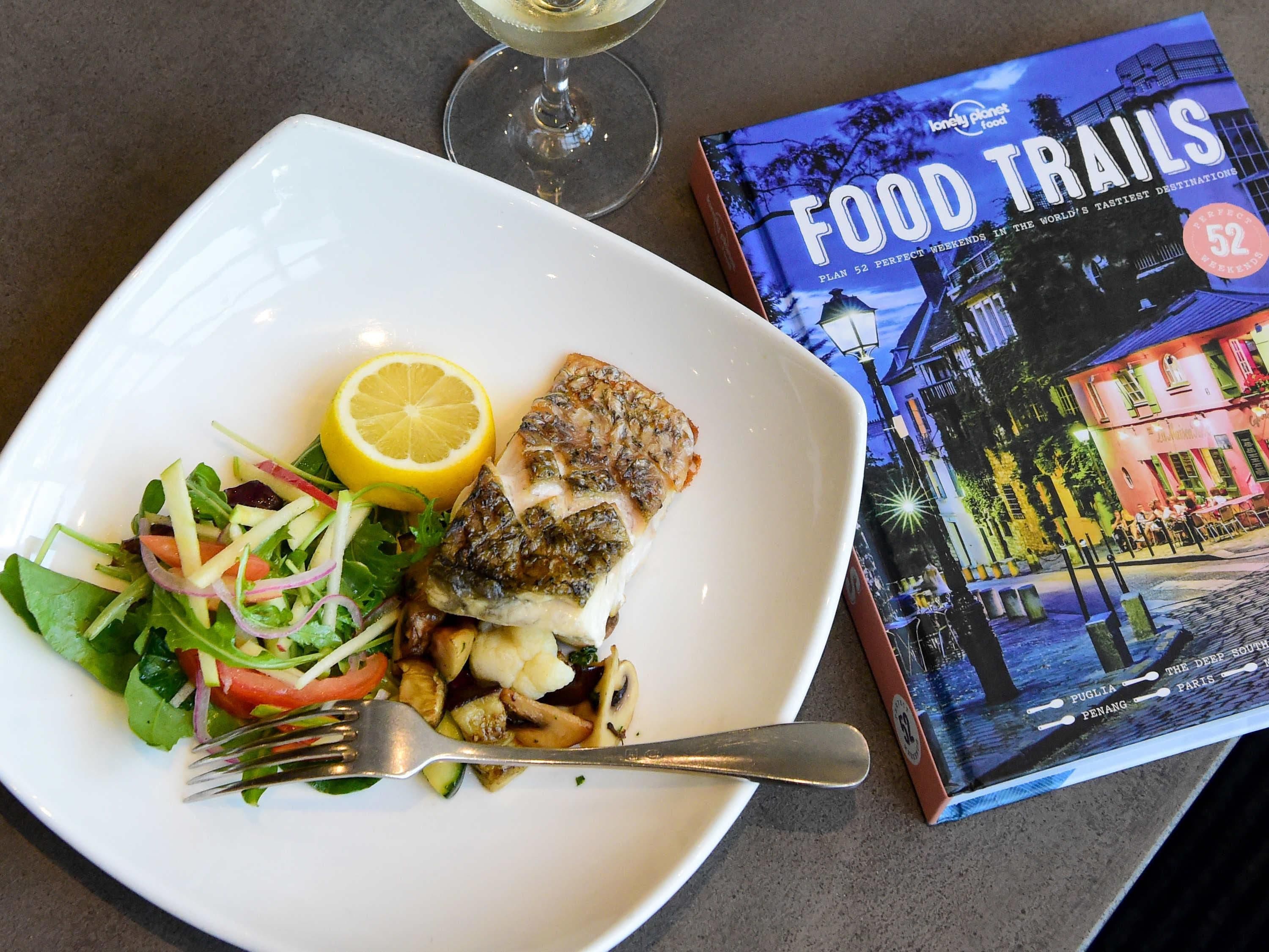A plate with fish, salad, and lemon, and a book titled 'FOOD TRAILS'.