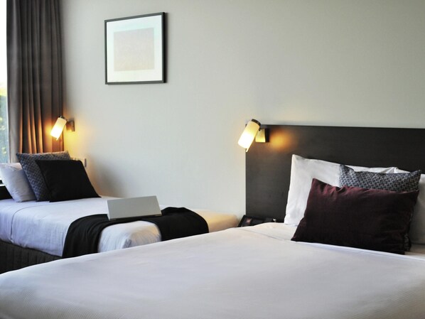 A hotel room with two beds, a laptop on one bed, and two wall-mounted lamps.