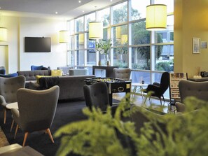 Un espace de détente moderne, doté de sièges confortables, d’une table de baby-foot et de grandes fenêtres offrant une vue sur l’extérieur.