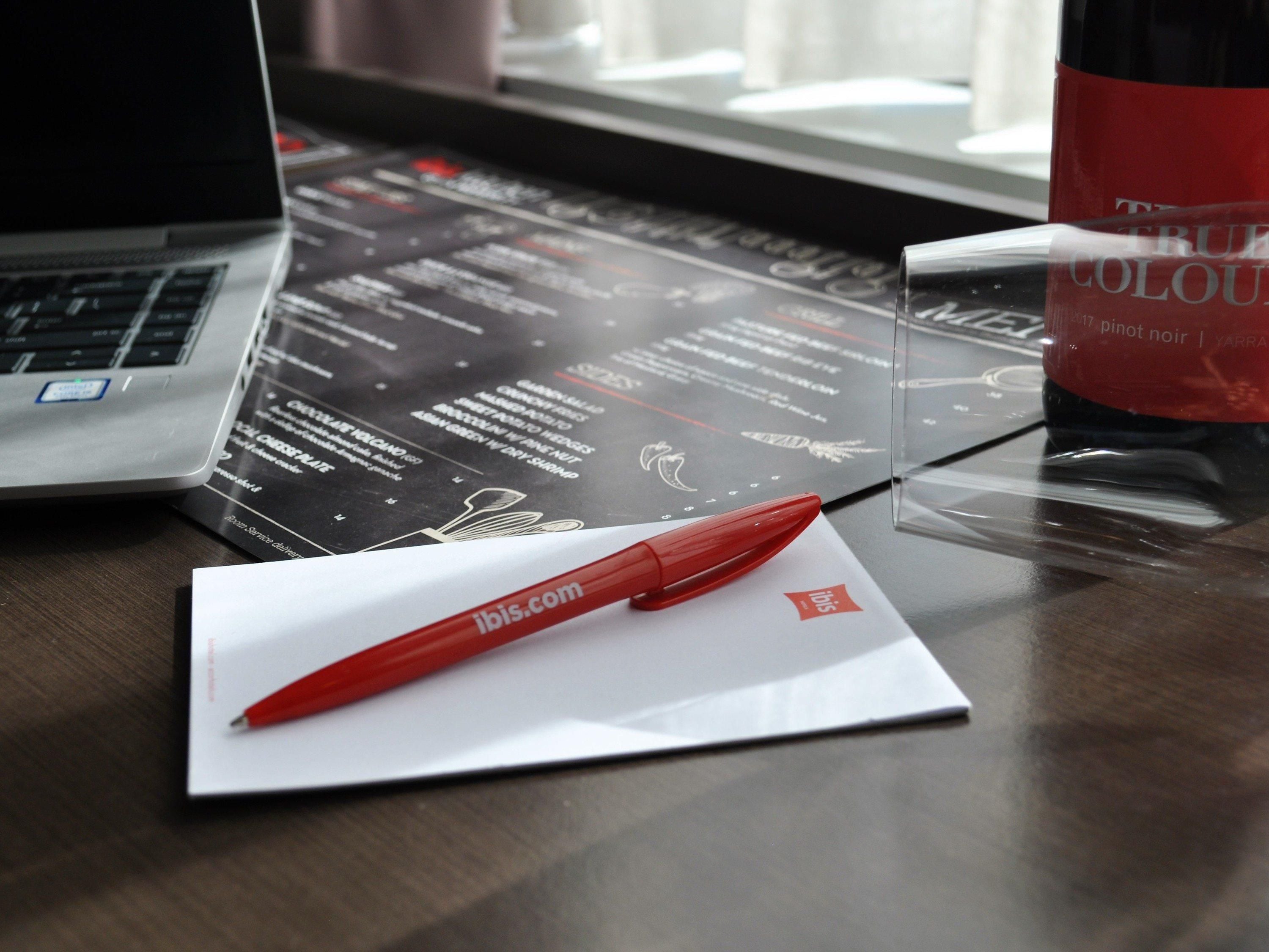 A laptop, a red pen, and a bottle on a table with printed material.