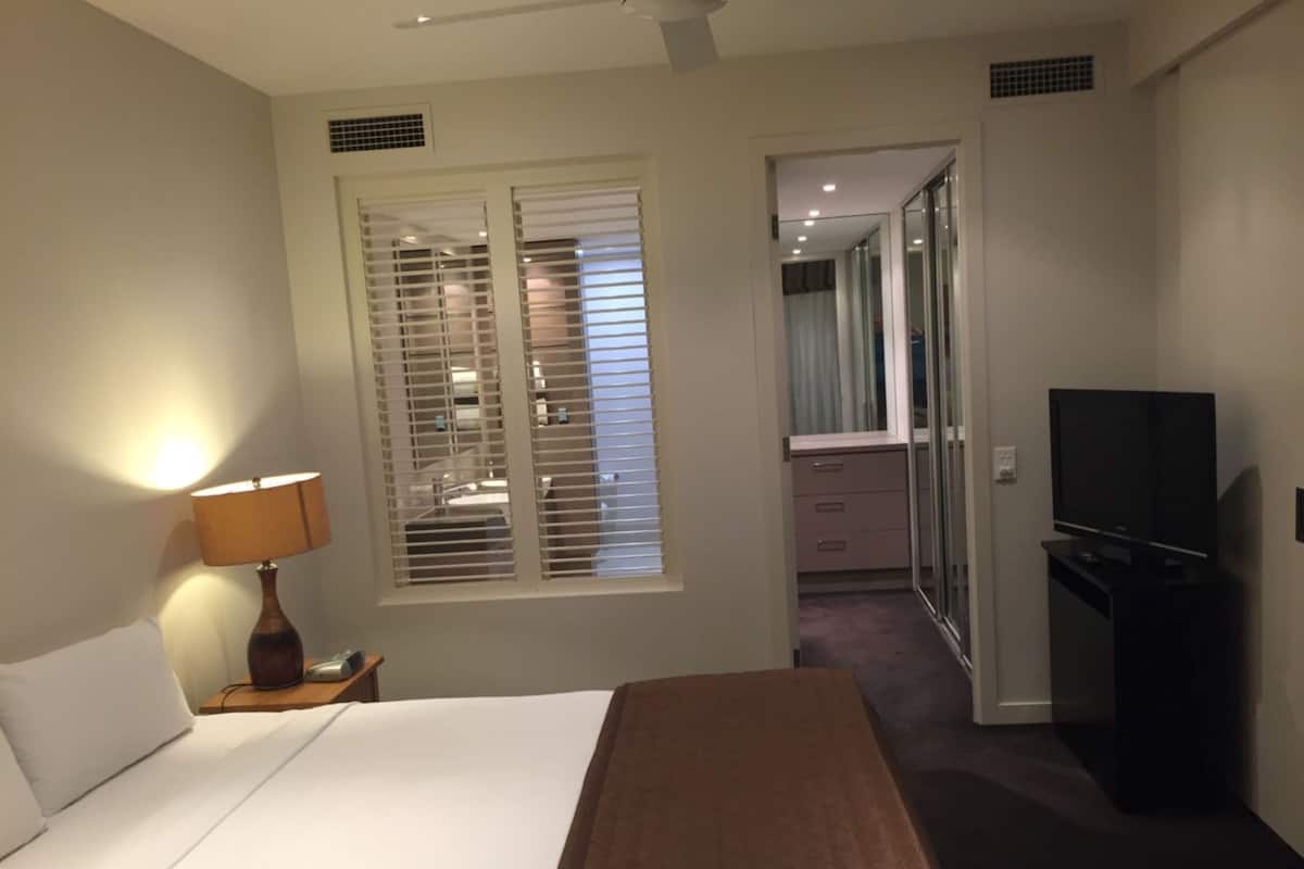 A hotel room with a bed, a TV, a lamp, and a bathroom visible through a door.
