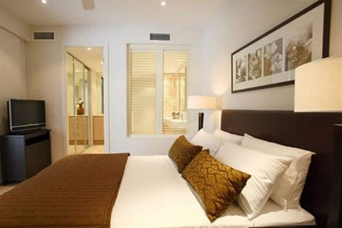 A hotel room with a bed, a television, a window with blinds, and a framed picture on the wall.