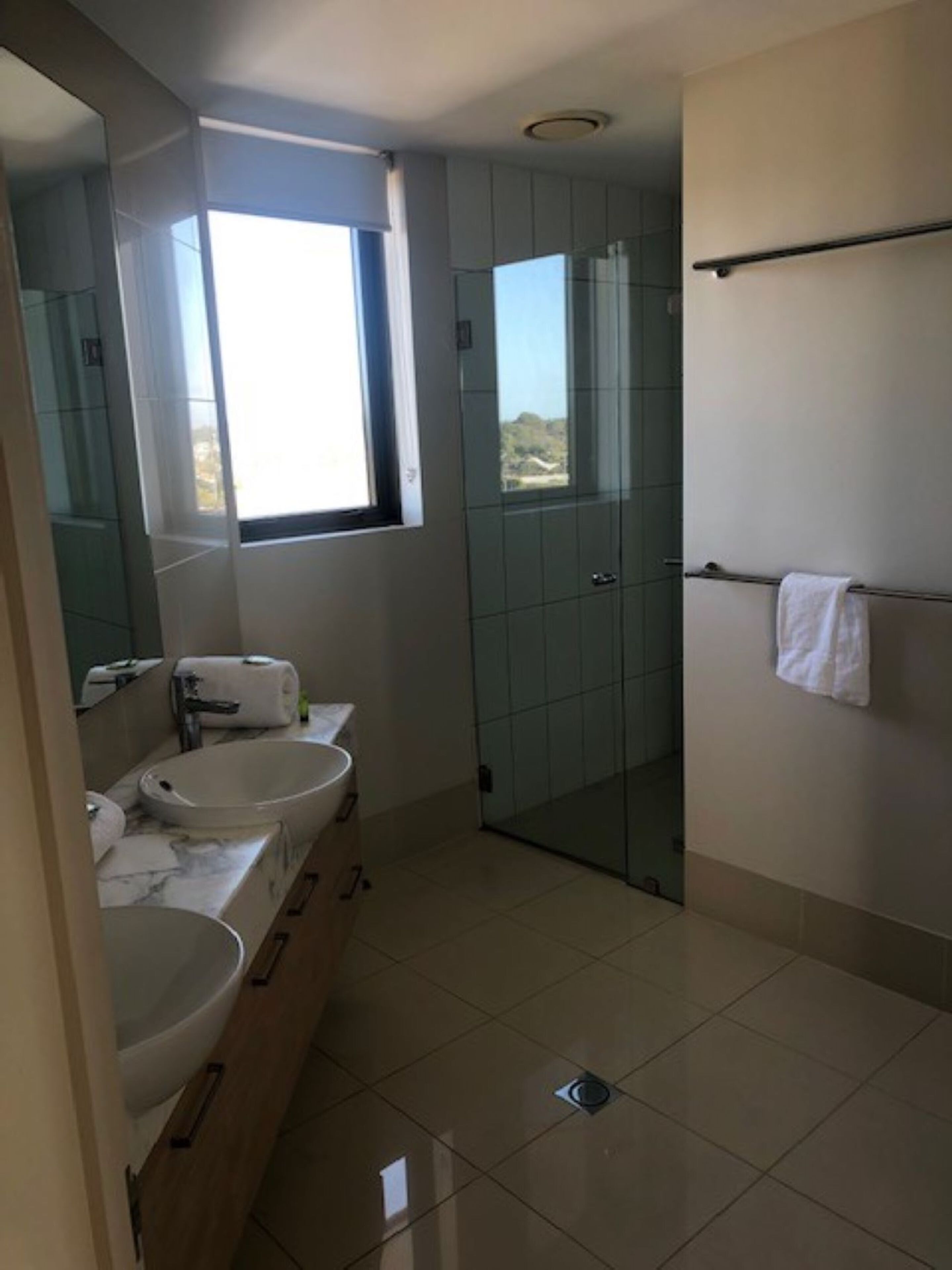 Un baño moderno con un espejo grande, dos lavamanos, una ducha y una ventana que proporciona luz natural.