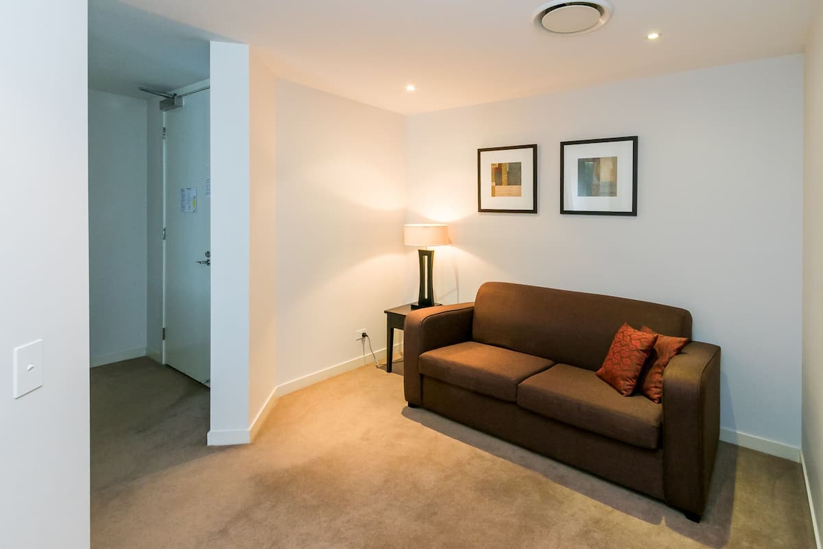 A room with a brown sofa, a standing lamp, and two framed pictures on the wall.