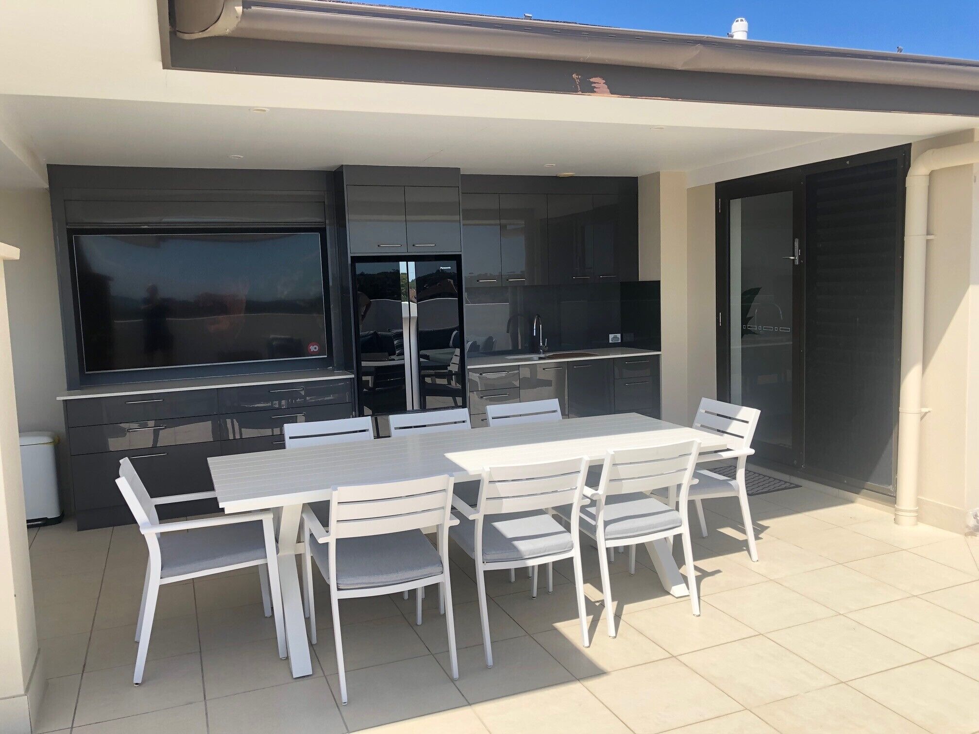 An outdoor dining area with a TV, kitchen, and sliding glass door.
