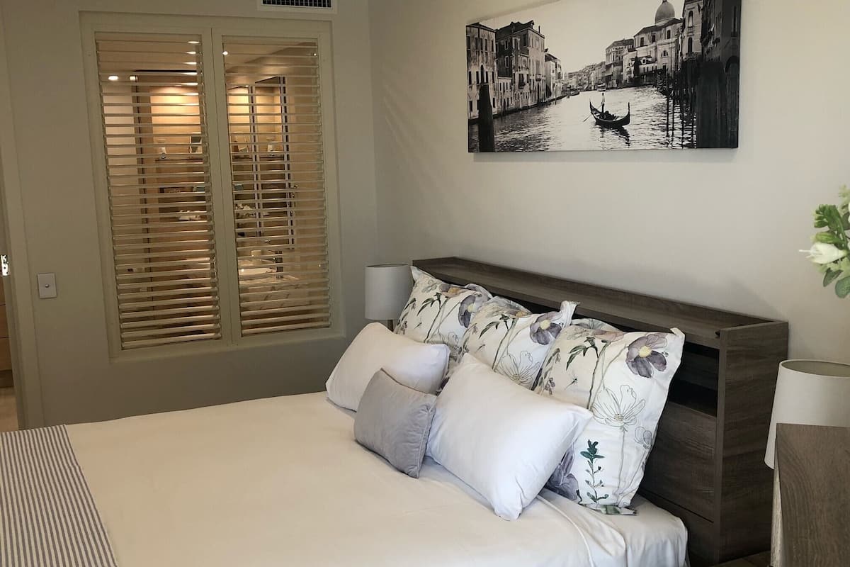 A bedroom with a bed, a nightstand, a lamp, and a painting of a canal scene.