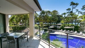 Un balcón con vistas a una piscina, sillas de descanso y palmeras.